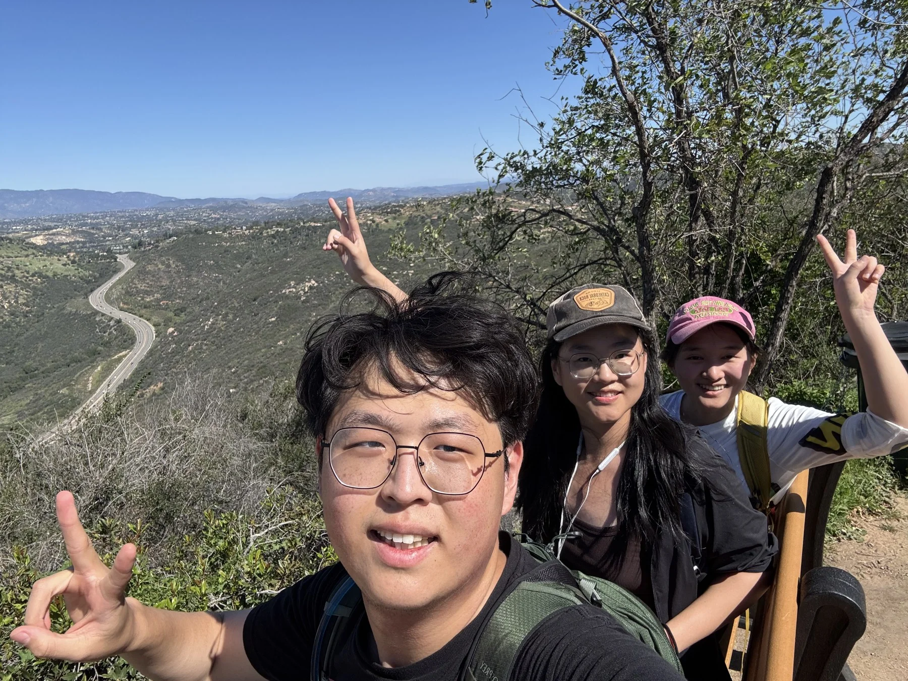 Hejia and friends making peace signs above a sunlit valley