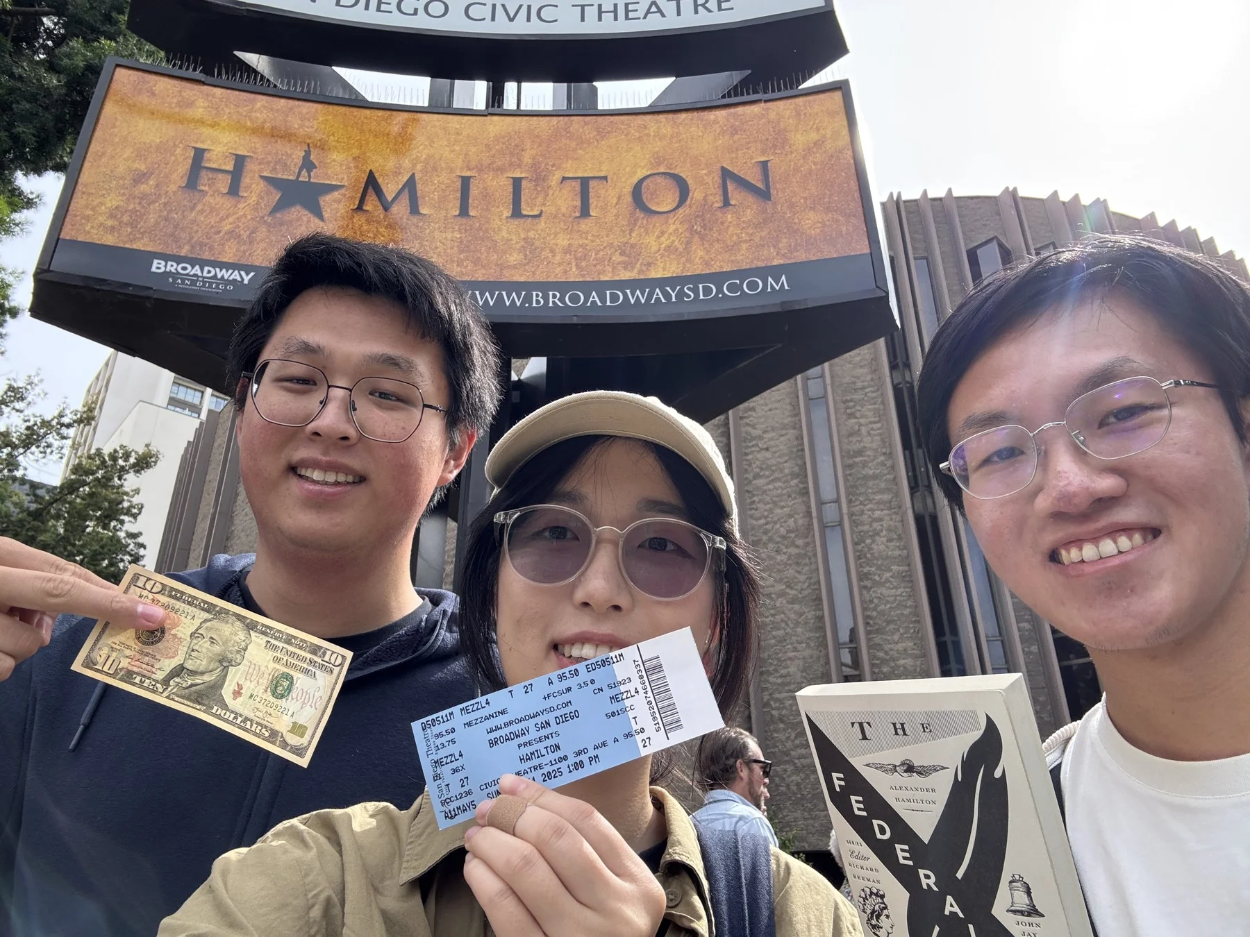 Three friends holding Hamilton tickets outside the San Diego Civic Theatre